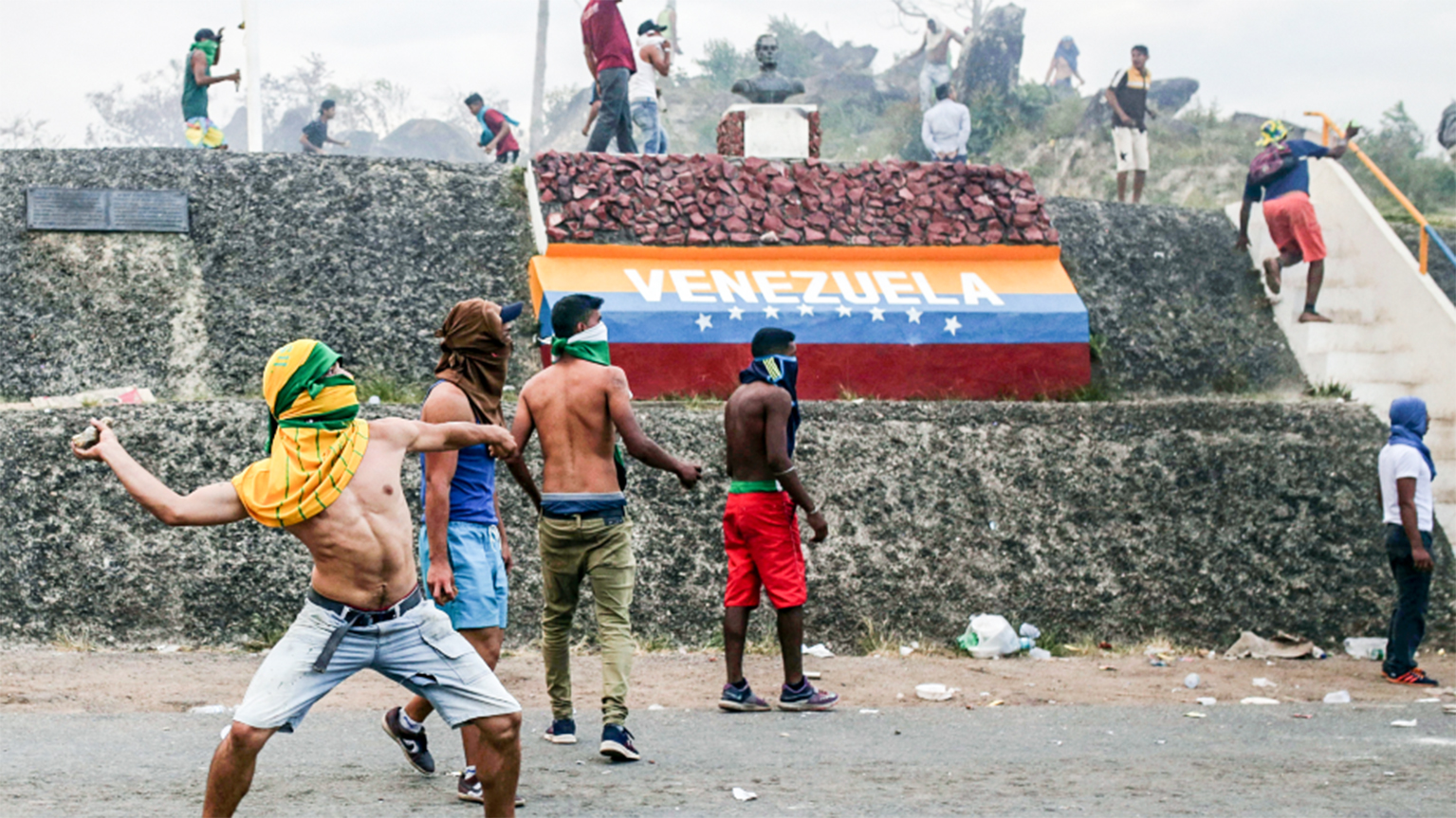 Người biểu tình Venezuela ném đá vào lực lượng an ninh tại biên giới nước này với Brazil hôm 23-2. Ảnh: AP