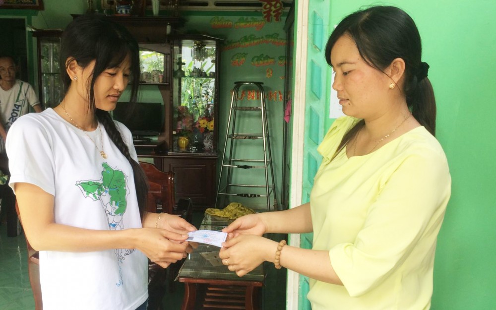 Đại lý thu BHYT ở xã Vĩnh Bình, huyện Vĩnh Thạnh (bên phải) trao thẻ BHYT cho người dân.