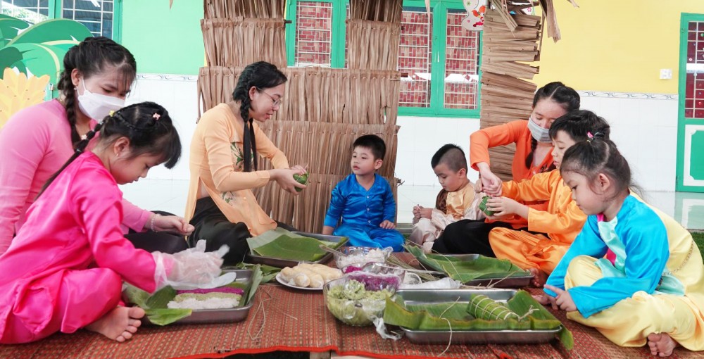 Các bé hào hứng trải nghiệm gói bánh tét với sự chỉ dẫn của cô giáo.